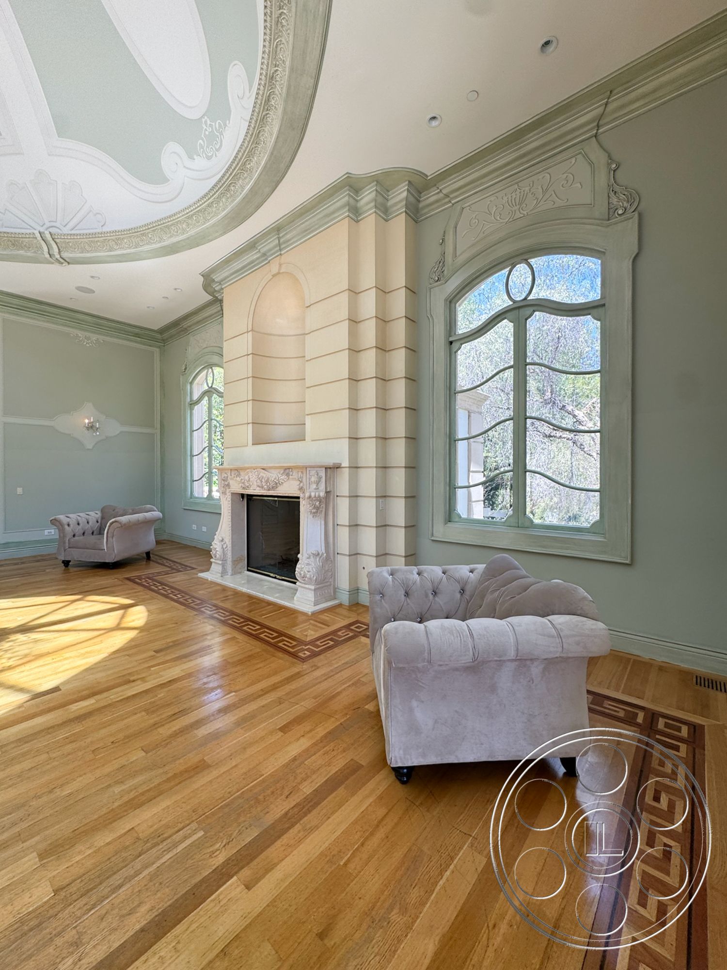 Tiffany Estate - exposed wood ceiling beams, hardwood living room floors, chandelier lighting fixture, decorative wall moldings, arched window frames, light green painted walls, ornate plaster ceiling details, carved marble fireplace surround, tufted velvet armchairs, geometric patterned inlay