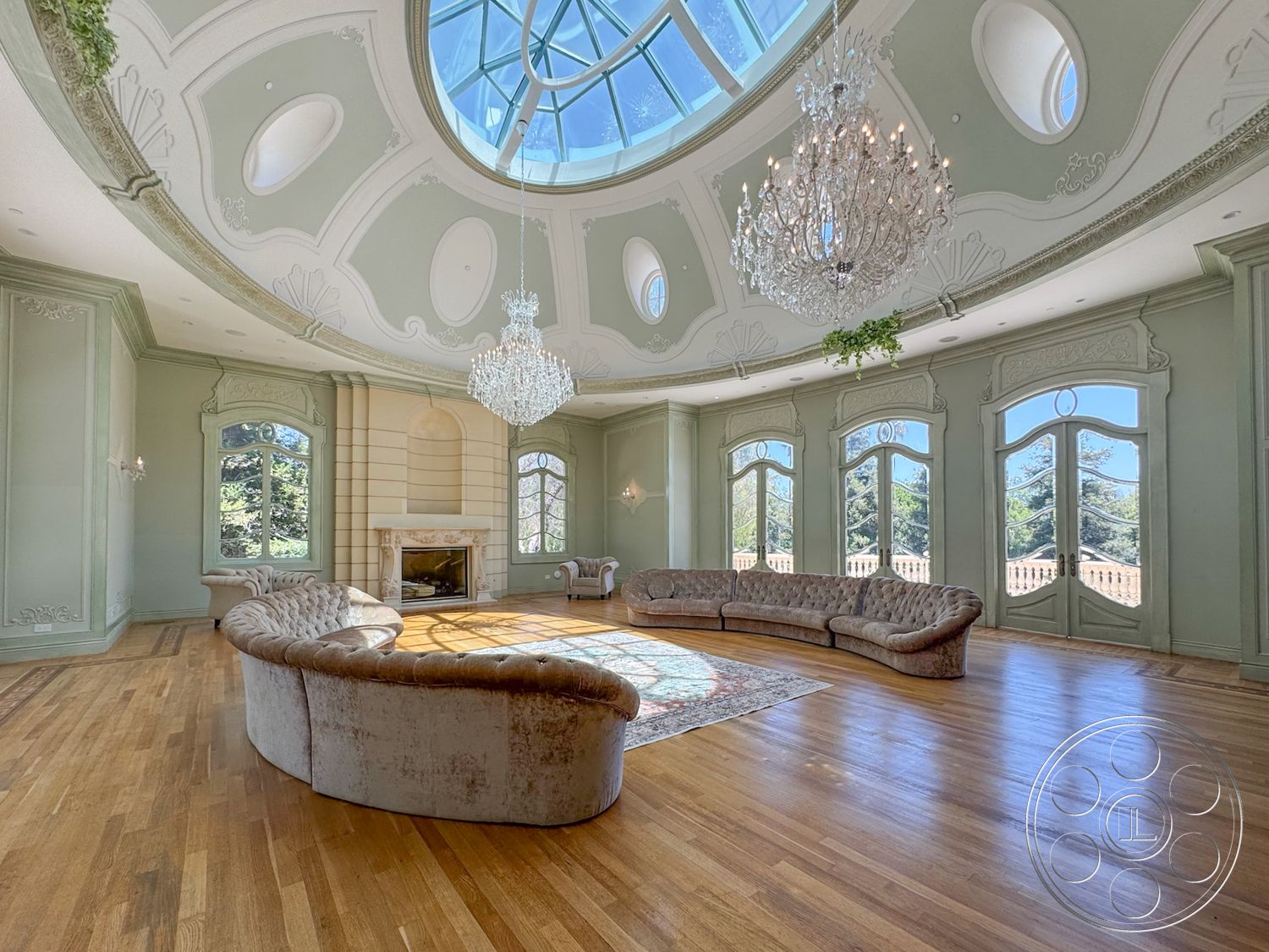 Tiffany Estate - crystal chandelier, large arched windows, area rug with intricate patterns, hardwood living room floors, exposed brick fireplace surround, classical architectural details, vaulted ceiling with decorative moldings, table chandelier, circular domed ceiling with skylight, lavender painted walls, soft upholstered sectional sofas