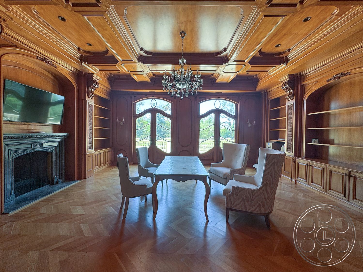 Tiffany Estate - coffered ceiling, upholstered chairs, large arched windows, ornate chandelier, elegant dining table, stone fireplace surround, wood paneling walls, herringbone hardwood flooring, built-in wooden cabinets