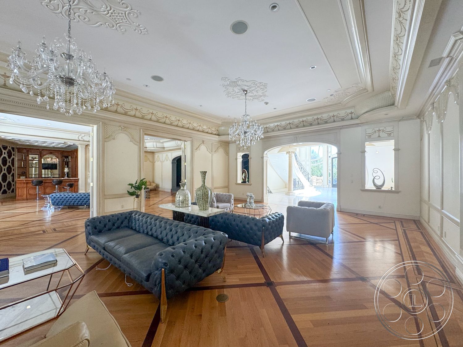 Tiffany Estate - natural light, glass coffee table, crystal chandelier, arched doorways, wood parquet flooring, crown molding details, decorative wall niches, intricate ceiling moldings, tufted velvet sofas, expansive living room, dark wood bar cabinetry
