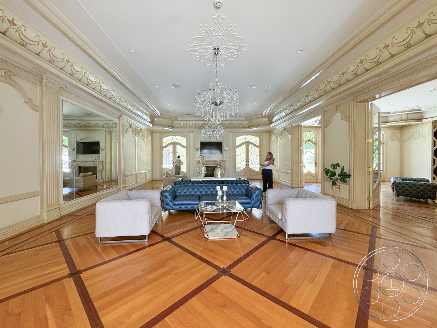 Tiffany Estate - open floor plan, arched doorways, decorative chandelier, hardwood living room floors, white painted walls, stone fireplace surround, intricate crown molding details, modern glass coffee table, elegant interior design, blue tufted leather sofa, mirrored accent walls, geometric patterns on flooring