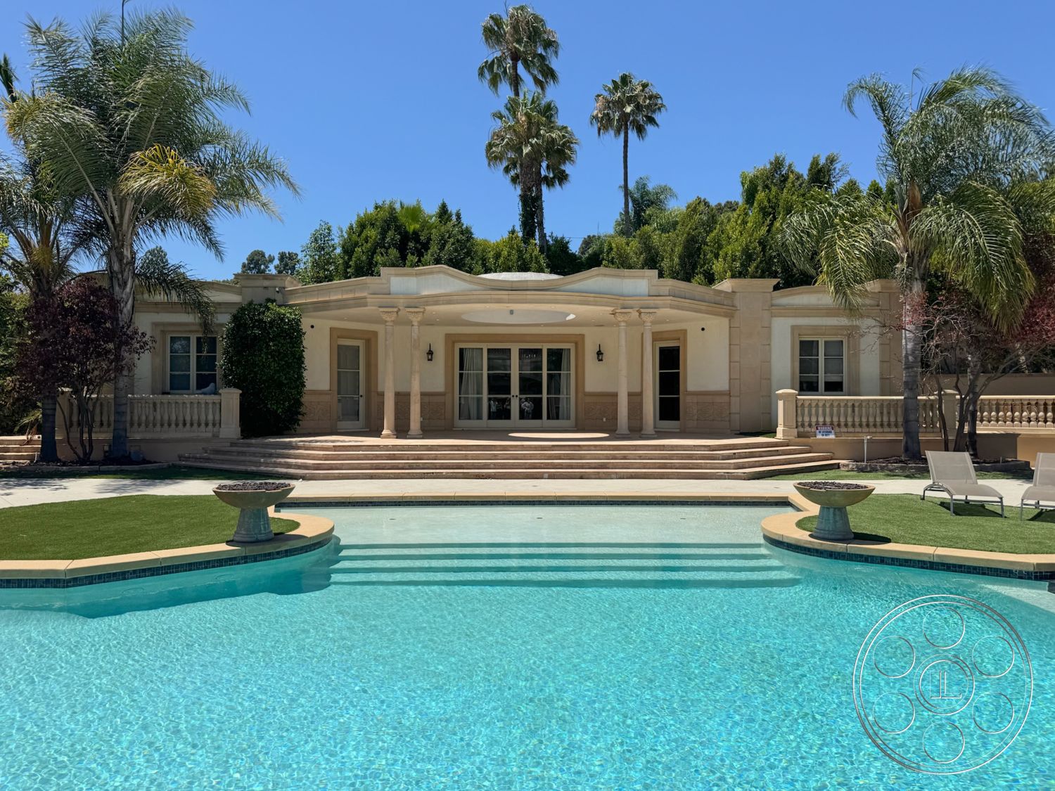 Tiffany Estate - exterior, rectangular swimming pool, landscaped lawn, arched doorways, tropical palm trees, textured exterior wall, paver stone patio, stucco exterior walls, concrete pool border, double glass doors, columned porch entry, beautiful garden setting