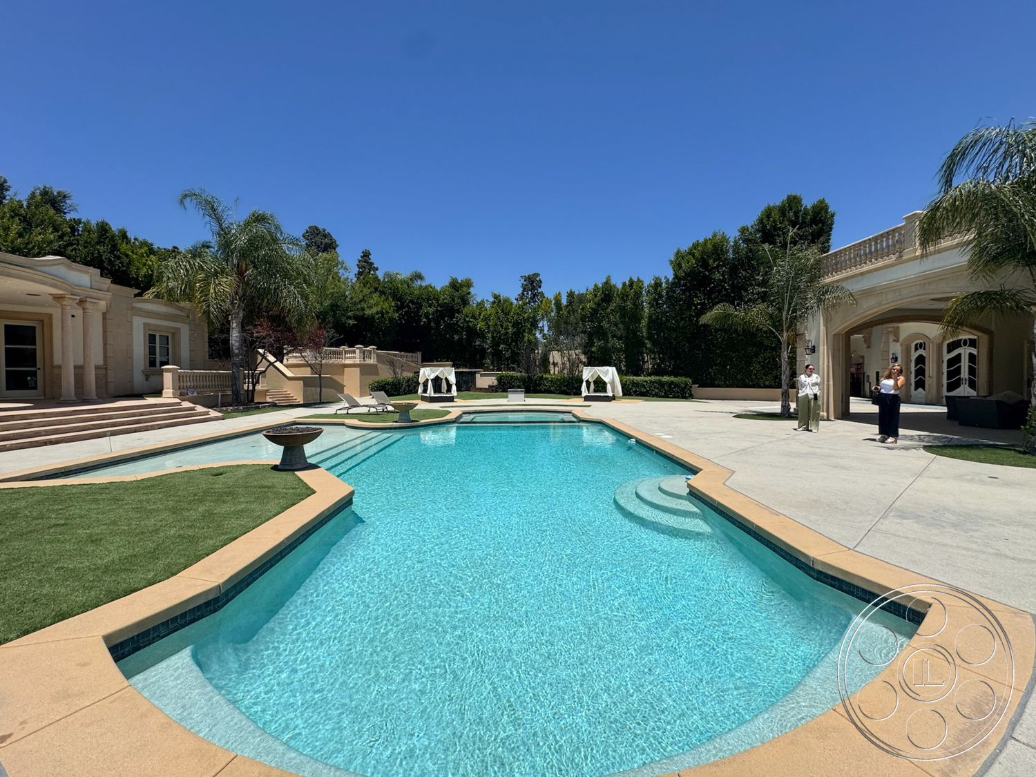 Tiffany Estate - exterior, palm trees, outdoor seating area, landscaped yard, support columns, arched doorways, rectangular pool, staircase with stone steps, concrete pool border, concrete patio floor, tile pool deck, stone water feature