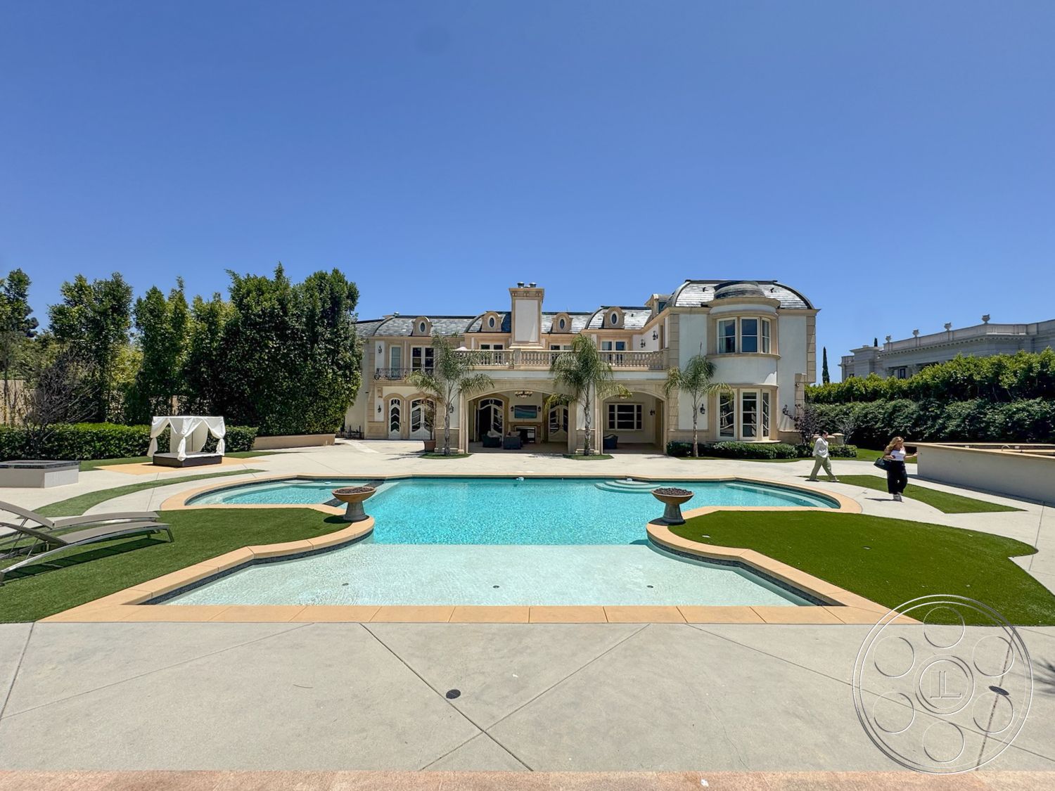 Tiffany Estate - exterior, palm trees, floor-to-ceiling windows, poolside lounge chairs, arched windows, traditional architectural style, rectangular pool, lush green landscaping, stone pool deck, concrete pool border, concrete patio floor, touch of artificial grass, multi-story mansion, detailed molding on facade, stately columns, ornate balcony