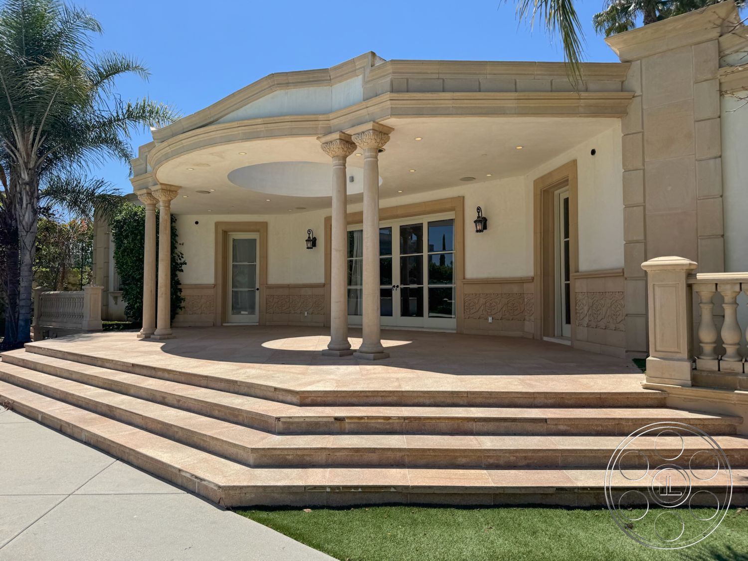 Tiffany Estate - exterior, textured wall panels, arched entryway, decorative wall molding, landscaped garden area, crown molding details, sunlit outdoor space, double glass doors, palm tree accents, sandstone patio flooring, round column supports, ornate balustrade, layered stone steps