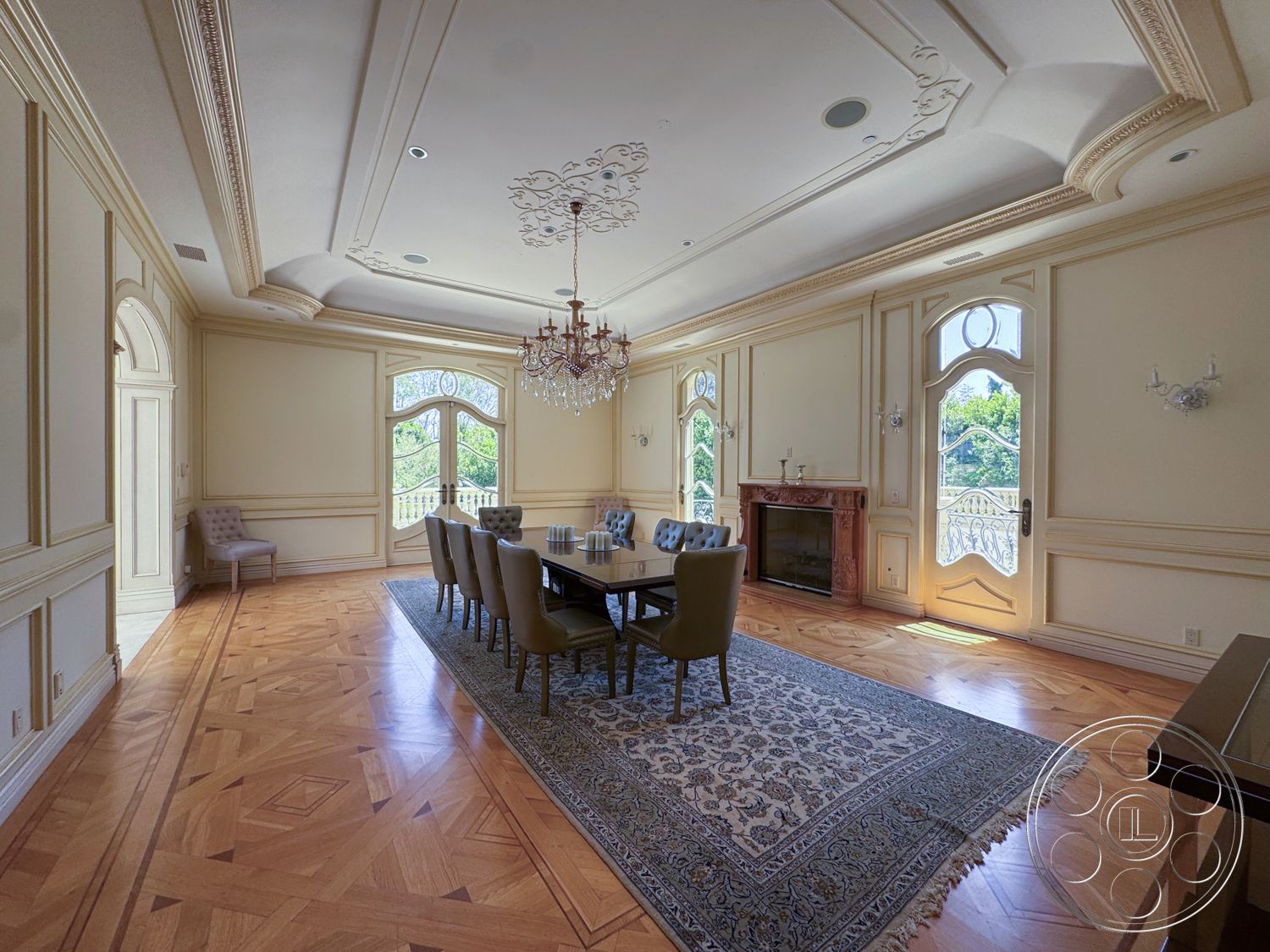 Tiffany Estate - upholstered dining chairs, wall sconces, natural light from windows, ornate chandelier, view of outdoor greenery, marble fireplace surround, arched windows with decorative trim, herringbone hardwood flooring, intricate crown molding details, cream painted walls, coffered dining room ceiling, classic dining table, fine area rug, elegant decorative wall panels