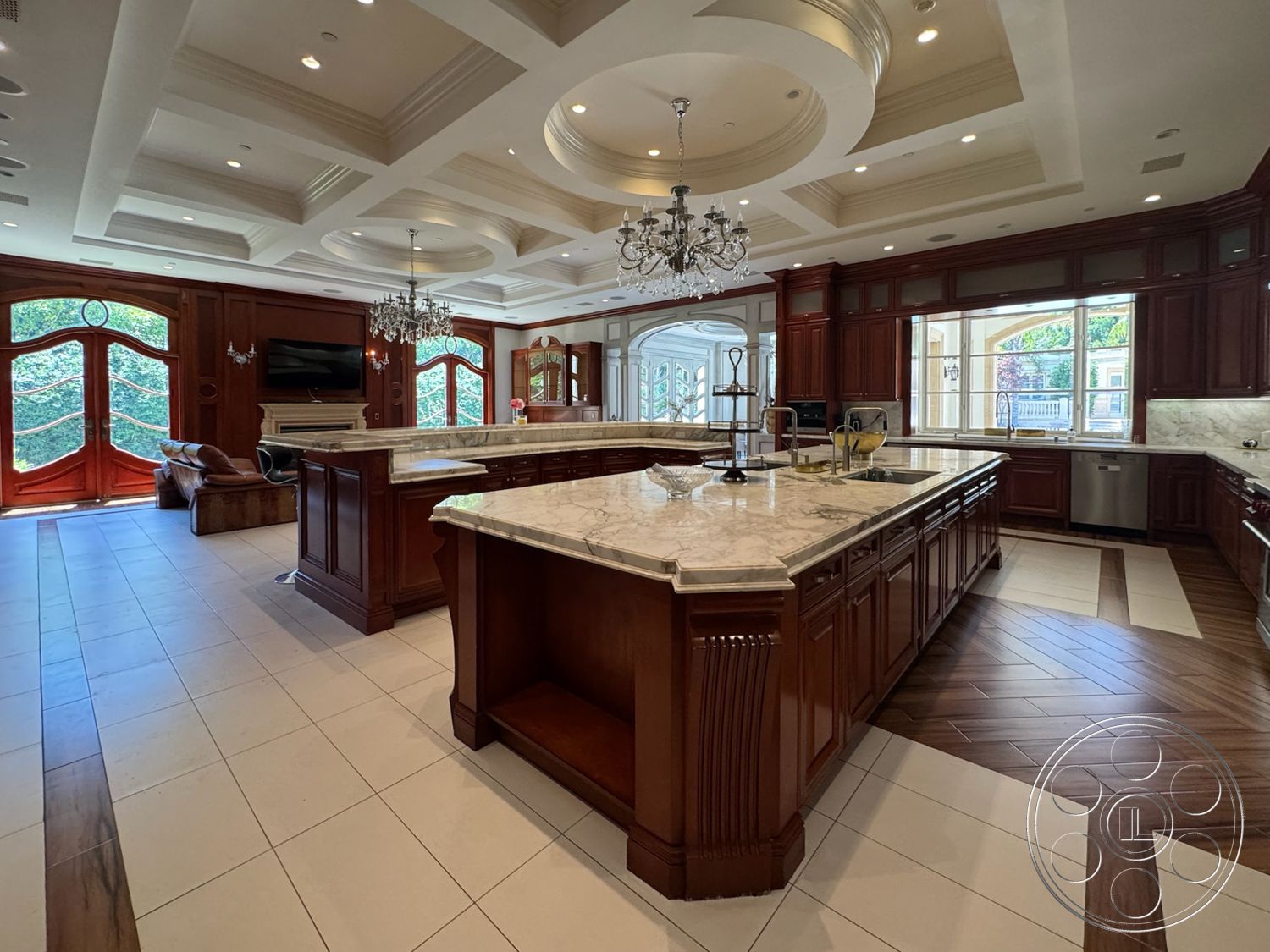 Tiffany Estate - open floor plan, double wooden front doors, large arched windows, cherry wood cabinetry, granite kitchen countertops, coffered ceiling details, marble kitchen island, modern chandelier lighting, tile kitchen flooring, sitting area with upholstered furniture, elegant kitchen design
