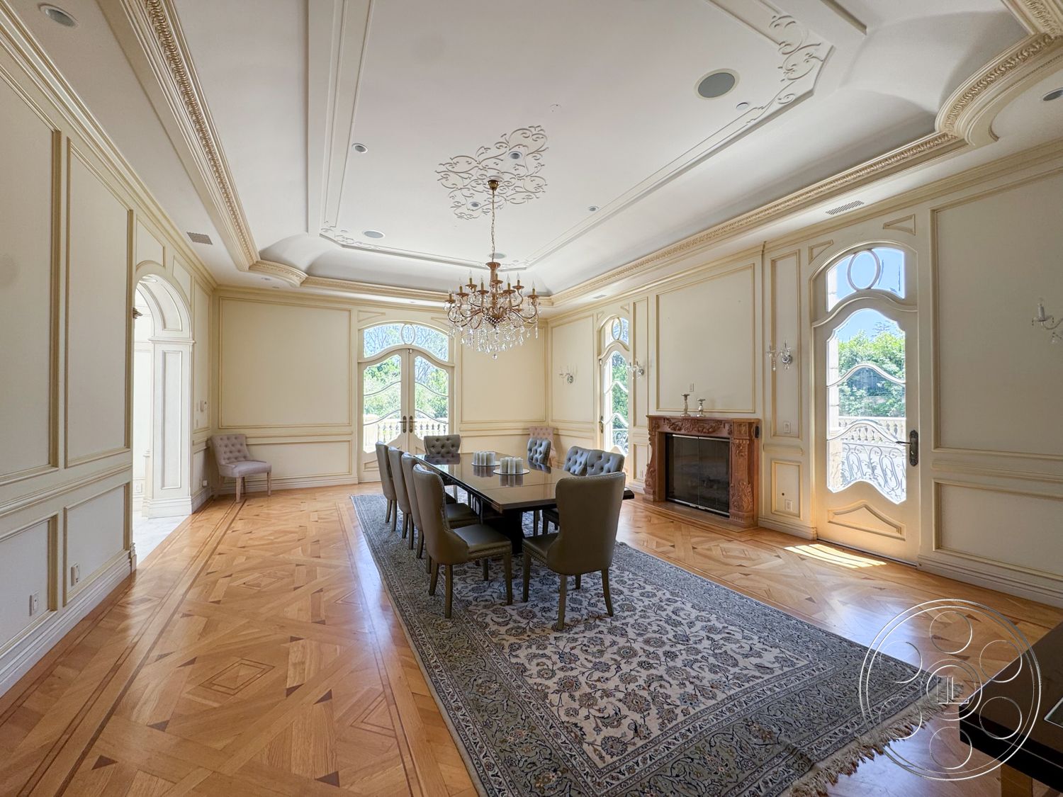 Tiffany Estate - decorative area rug, open floor plan, arched doorways, natural light from windows, large arched windows, wood parquet flooring, exposed brick fireplace surround, neutral painted walls, chandelier lighting fixture, intricate crown molding details, plush upholstered dining chairs, coffered ceiling design, elegant dining room, ornate wall trim, dining table with additional seating