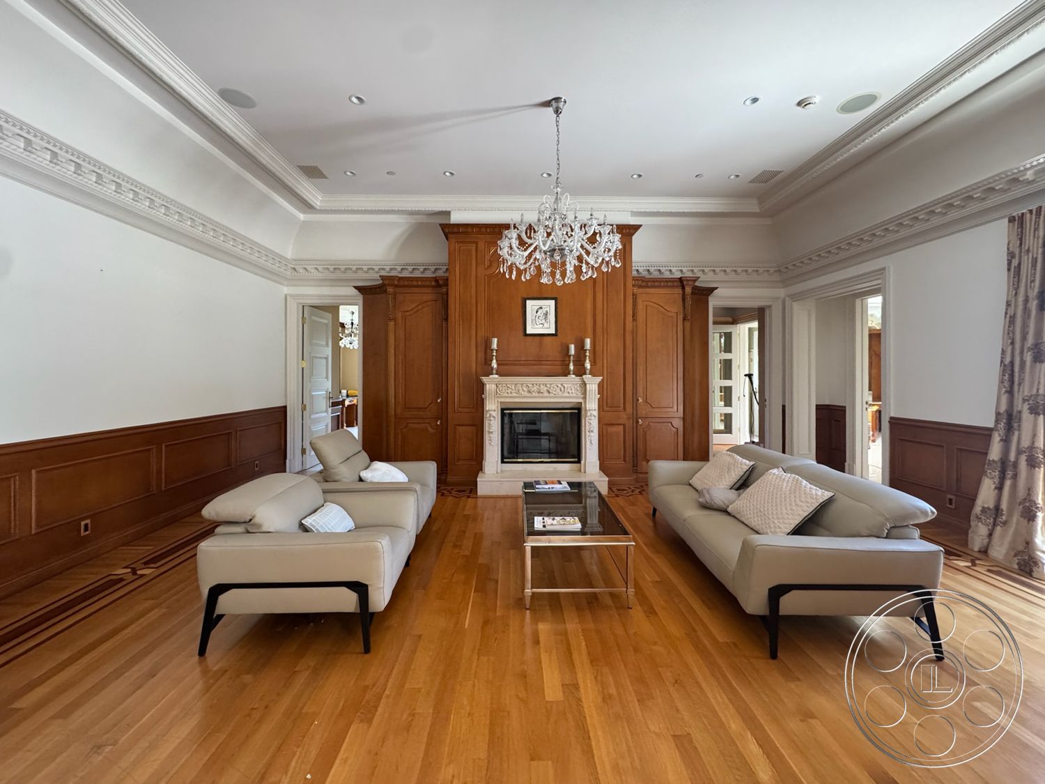 Tiffany Estate - glass coffee table, textured curtains, hardwood living room floors, marble fireplace surround, wood paneling walls, exposed wood crown molding, chandelier lighting fixture, sofa with upholstered cushions, doorway with detailed trim
