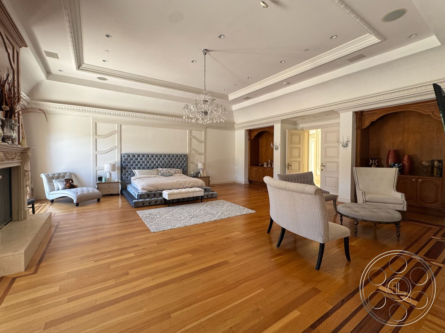 Tiffany Estate - decorative area rug, transom windows, traditional furniture, hardwood bedroom floors, marble fireplace surround, wood paneling accent wall, chandelier lighting fixture, textured white walls, coffered ceiling with crown molding, tufted upholstered bed