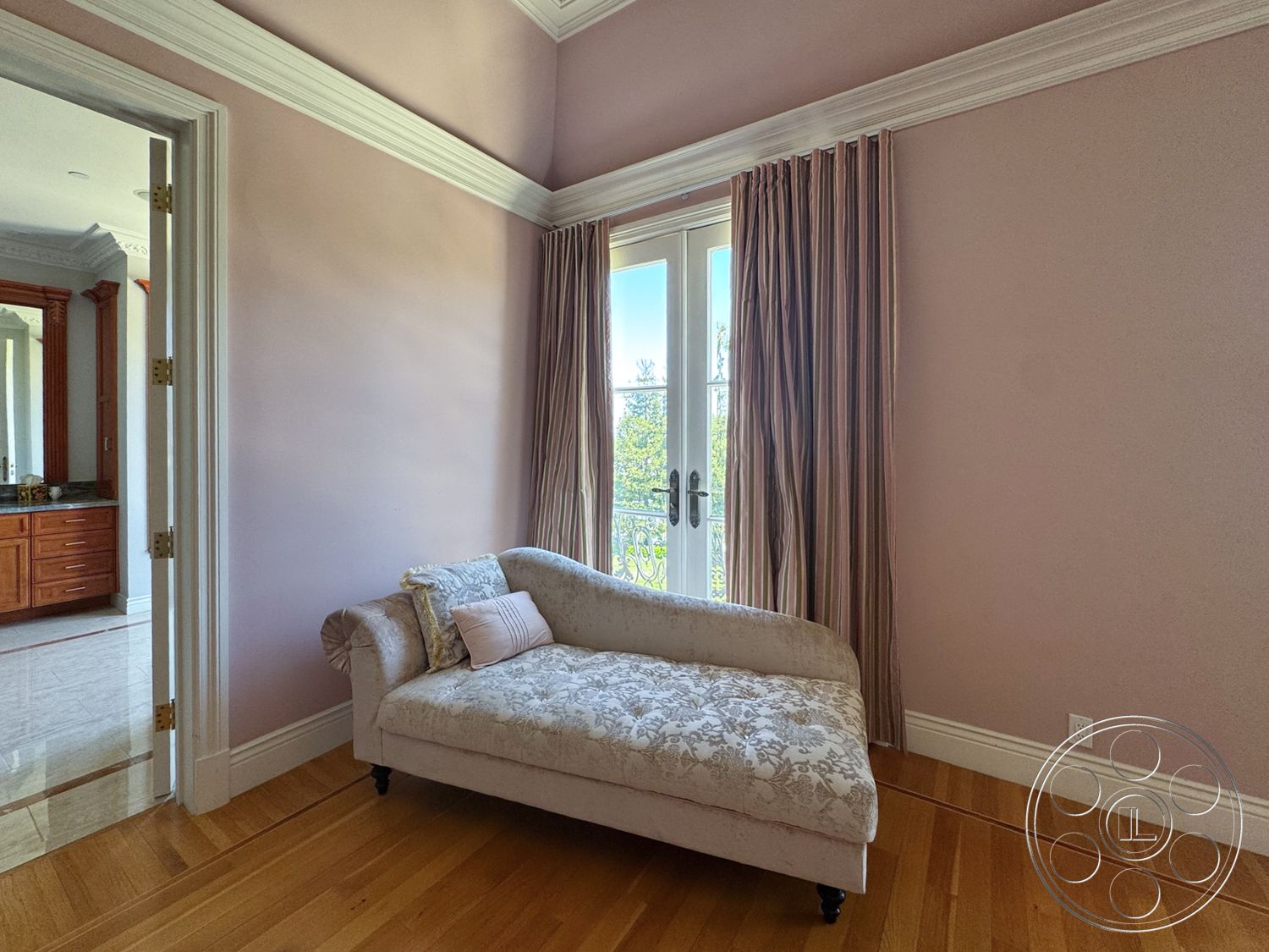 Tiffany Estate - natural light, hardwood flooring, decorative pillows, floor-to-ceiling windows, crown molding details, exposed wood baseboards, light pink painted walls, elegant door hardware, plush upholstered chaise lounge, sheer fabric curtains, ornate wood cabinetry in adjoining room