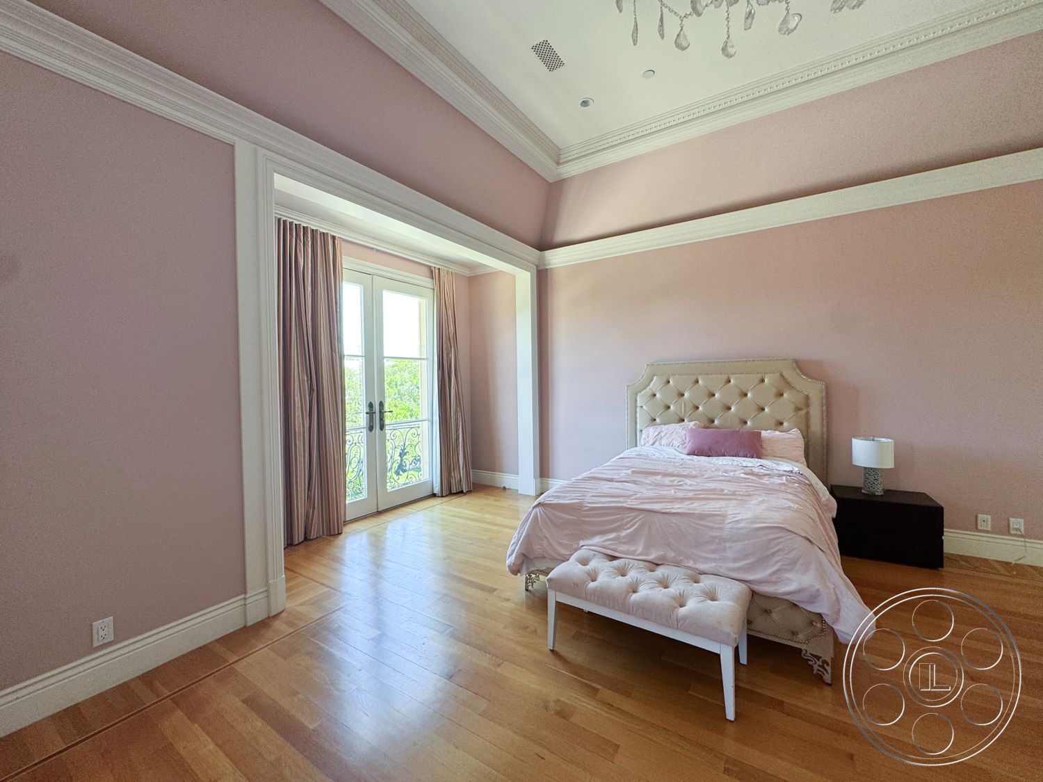 Tiffany Estate - floor-to-ceiling windows, light-colored curtains, hardwood bedroom floors, minimalist nightstand, crown molding details, modern bedside lamp, light pink painted walls, tufted upholstered headboard, white bedding with pink accents, double French doors with wrought iron railing