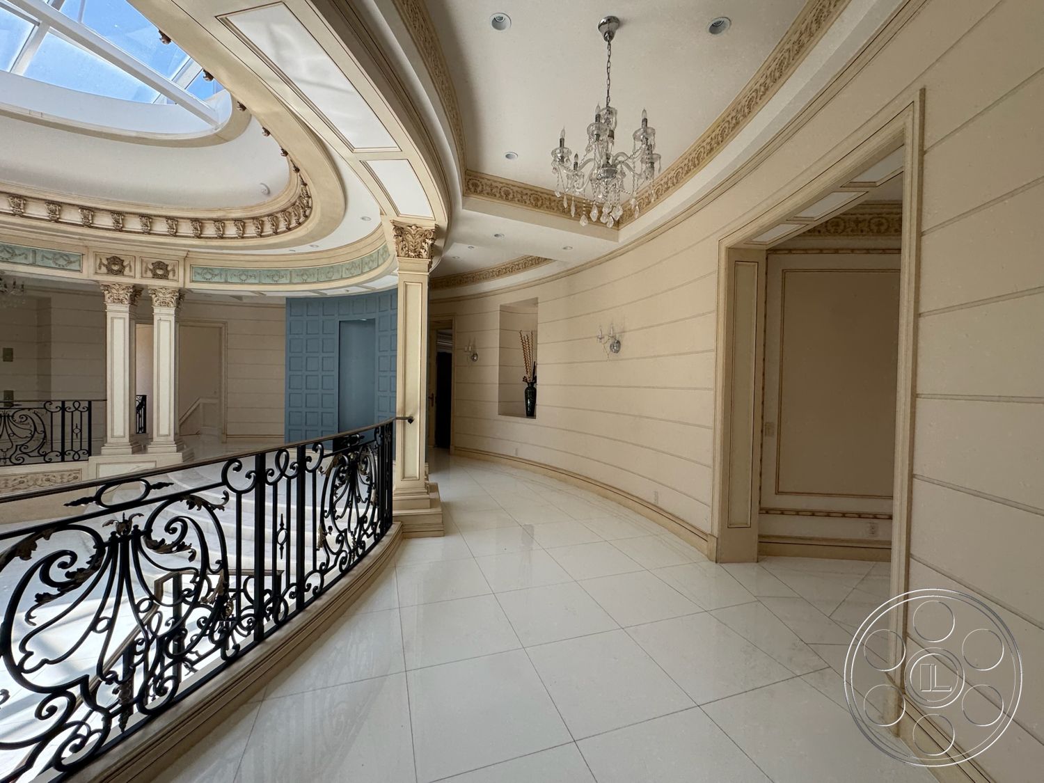 Tiffany Estate - black wrought iron railing, curved hallway, decorative wall paneling, natural light from skylight, marble floor tiles, chandelier lighting fixture, intricate crown molding, exposed column details, ornate ceiling detail, soft cream-colored walls, embellished door frames, elegant archway entry