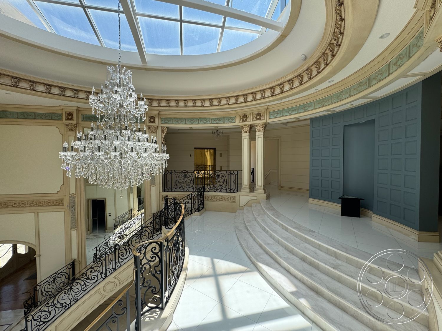 Tiffany Estate - chandelier lighting, polished marble flooring, architectural columns, decorative wall paneling, ornate ceiling moldings, cream-colored painted walls, light-filled entryway, intricate wrought iron railings, curved marble staircase, luxurious foyer design, large circular skylight, exposed plaster ceiling details, baroque-inspired architectural style