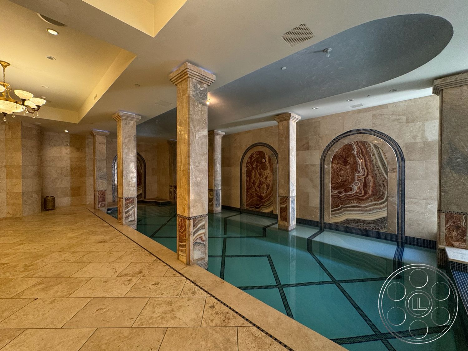 Tiffany Estate - vaulted ceiling, marble flooring, decorative tile border, exposed column structure, marble pool surround, stone feature walls, arched wall recesses, indoor pool area, modern luxury spa design