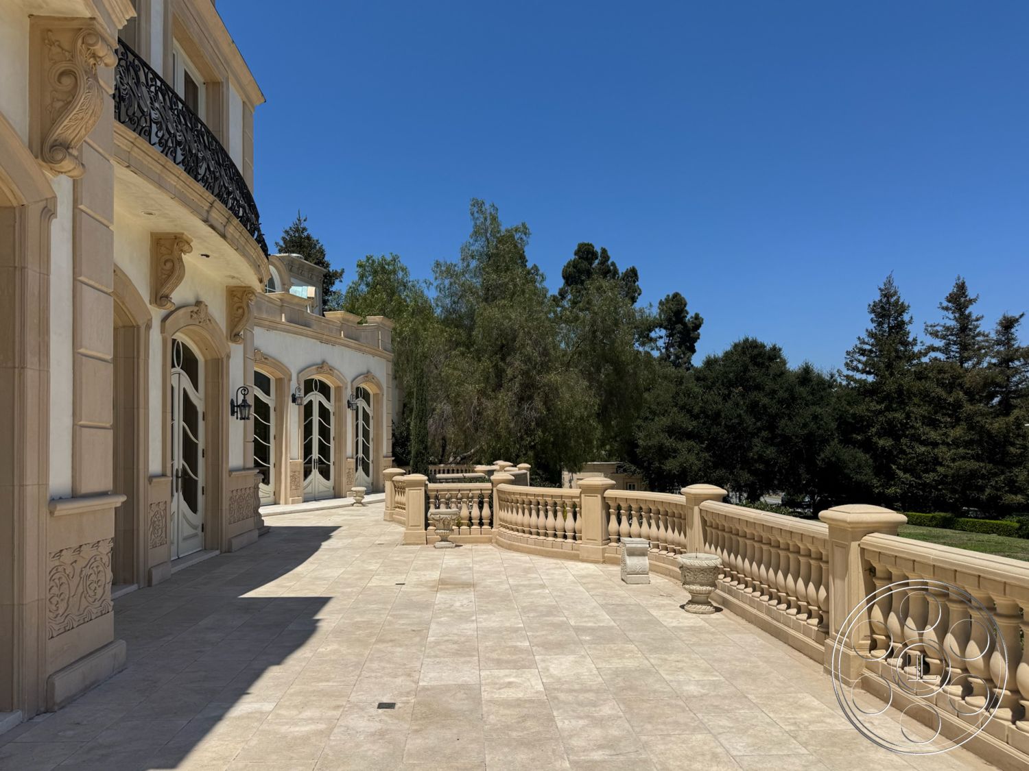 Tiffany Estate - exterior, elevated terrace, traditional architectural style, landscaped garden setting, arched windows with decorative trim, limestone patio flooring, balustrade terrace, plastered exterior walls, ornate wrought iron balcony railing, detailed cornice moldings
