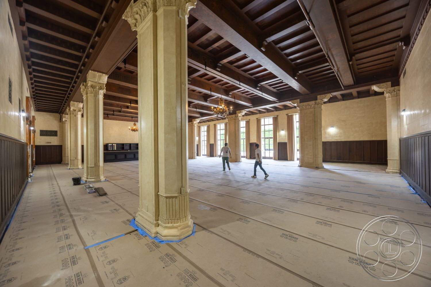 The Plaza - large windows, open floor plan, high vaulted ceiling, textured plaster walls, dark wood paneling, historic architectural details, traditional chandelier, exposed wooden ceiling beams, decorative plaster columns, softwood flooring underlayment