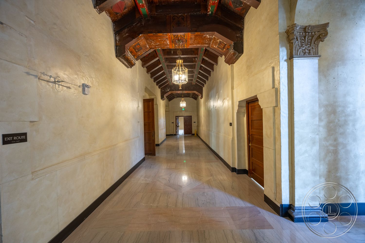 The Plaza - wooden doors, marble flooring, textured plaster walls, dark wood trim, interior hallway, traditional chandelier lighting, exposed wooden beams ceiling, ornate wood column details