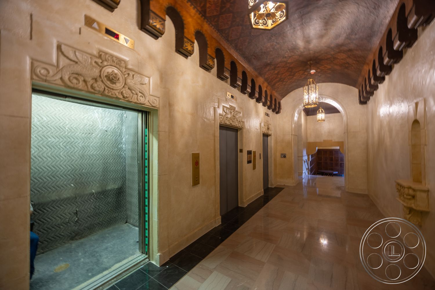The Plaza - textured wall accents, polished marble flooring, arched doorways, exterior hallway, ornate ceiling design, decorative plaster walls, elevator doors with ornate detailing, bronze light fixtures, open elevator shaft, wall-mounted decorative niches