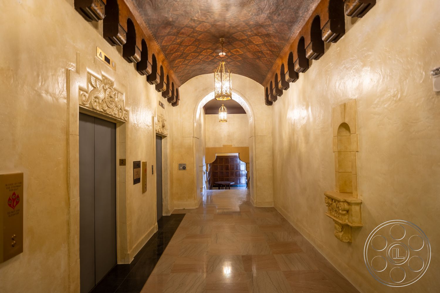 The Plaza - arched doorways, textured plaster walls, marble floor tiles, decorative wood trim, decorative ceiling with wood beams, elevators with metallic push buttons, ornate wall niches, vintage-style light fixtures, accent wall with decorative molding