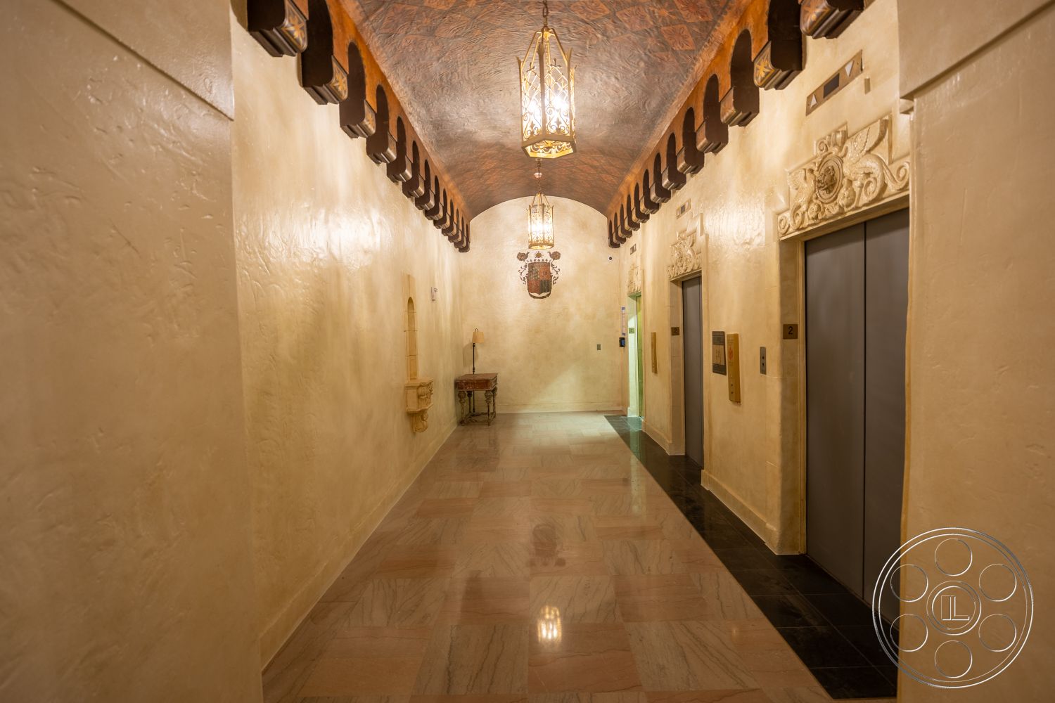 The Plaza - ornate light fixtures, textured plaster walls, arched ceiling, elevator access, interior hallway, wood beam ceiling, marble floor tiles, historical architectural details, decorative wall moldings