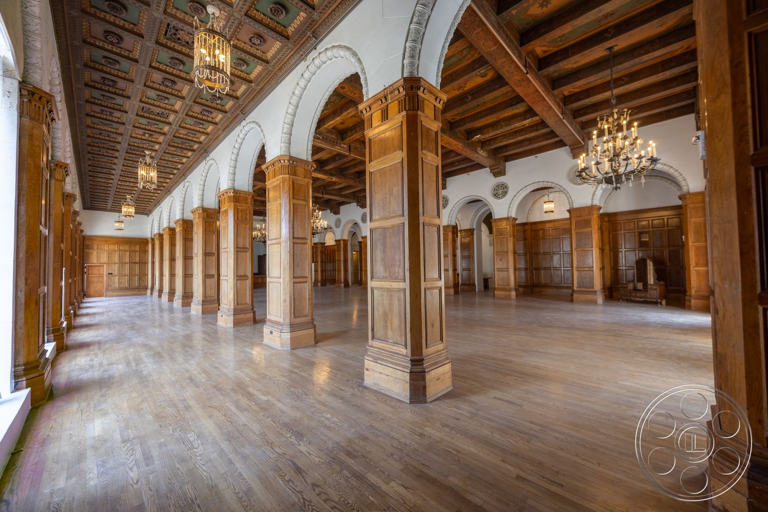 The Plaza - hardwood flooring, large open space, chandelier lighting, arched doorways, decorative molding details, exposed wooden ceiling beams, wood paneled walls, intricate ceiling detail, column-supported structure