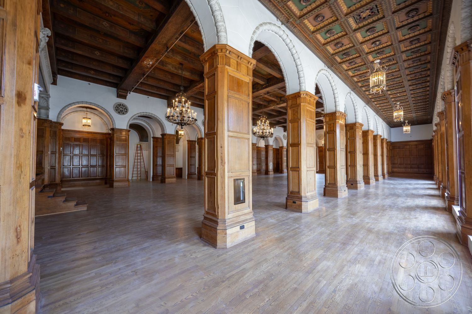 The Plaza - hardwood flooring, vaulted ceiling, chandelier lighting, arched doorways, ornate columns, traditional architectural style, spacious hall, exposed wood ceiling beams, wood paneling on walls, decorative plaster ceiling