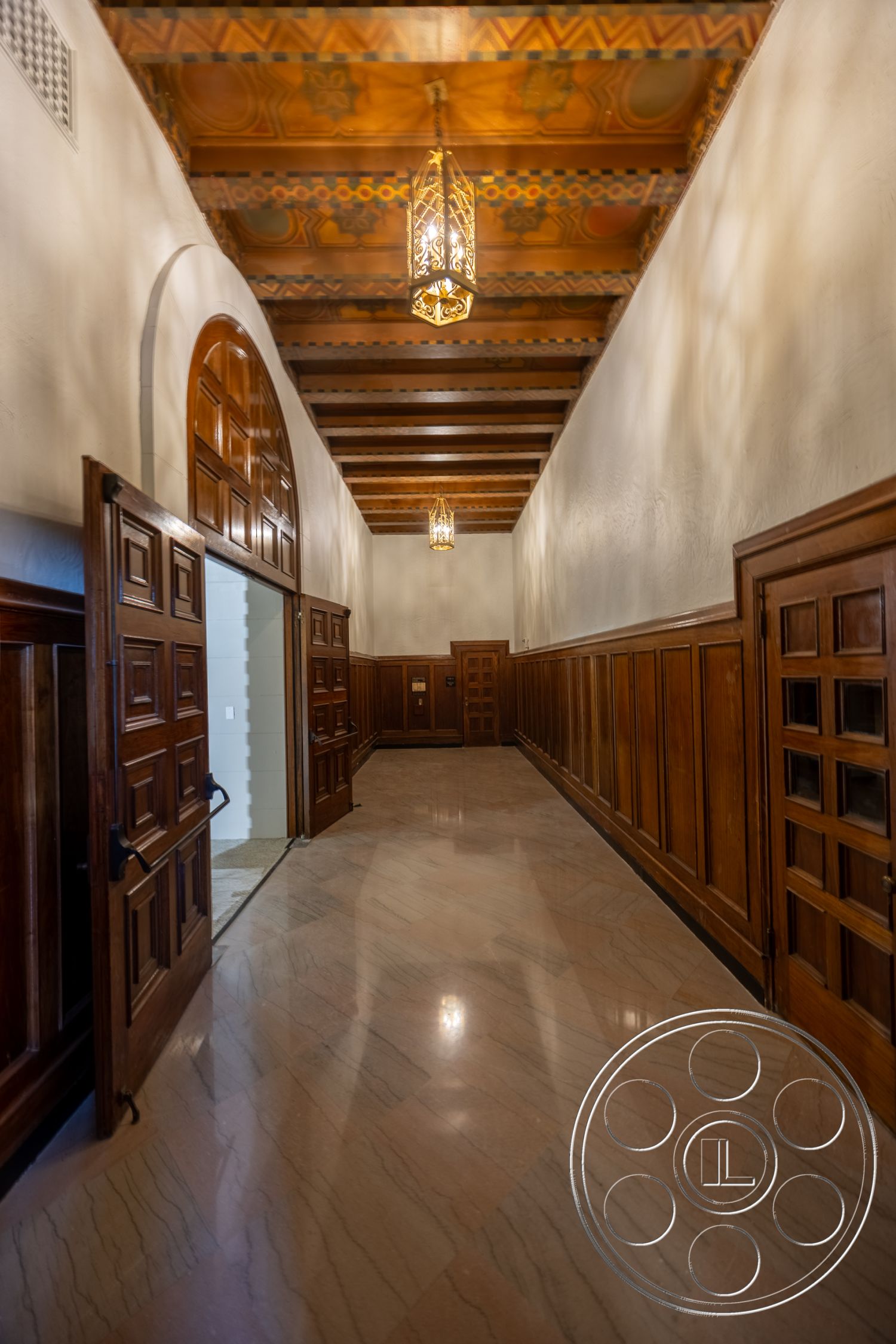 The Plaza - marble flooring, arched doorways, dark wood paneling, traditional architectural style, exposed wood ceiling beams, decorative ceiling details, polished marble hallway floor, ornate pendant lighting