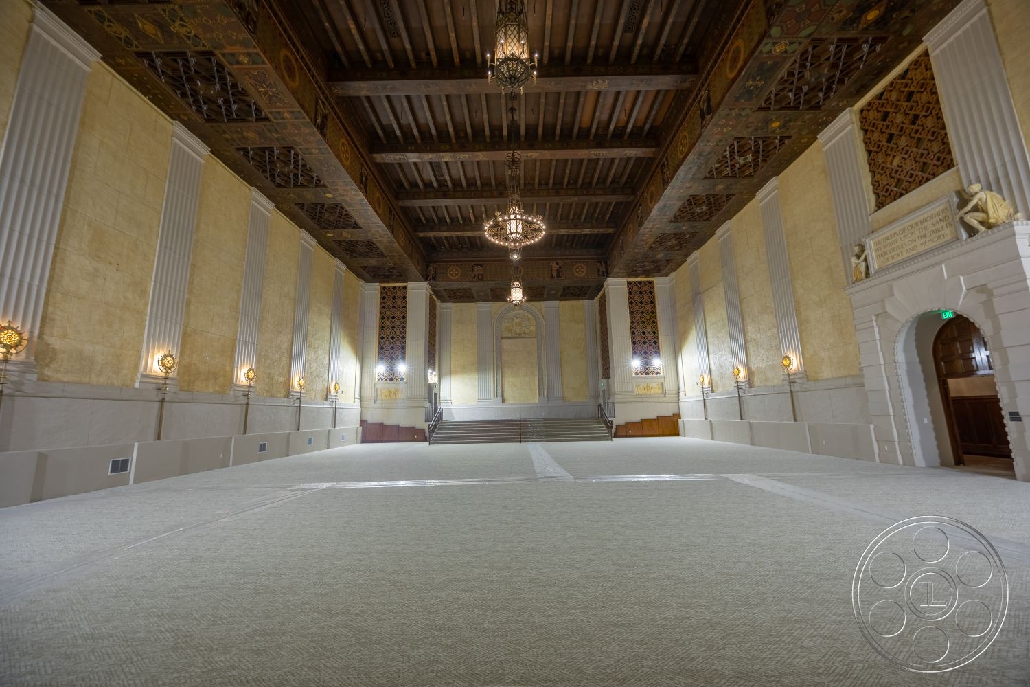 The Plaza - arched doorways, textured plaster walls, ornate wall sconces, elevated seating area, exposed wood ceiling beams, wood beam ceiling, classical architectural details, intricate ceiling moldings, marble staircase, gold leaf wall accents, chunky chandelier lighting, traditional theater-style seating area, checkerboard carpet flooring, large open space for events, elegant entry foyer