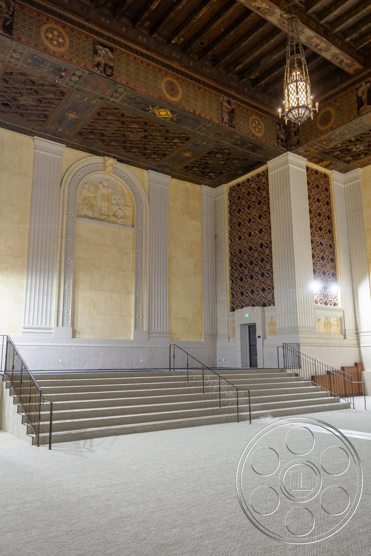The Plaza - carpet flooring, textured plaster walls, historic architectural details, exposed wood ceiling beams, metal stair railings, ornate coffered ceiling, intricate decorative ceiling tiles, light-colored plaster wall finish, architectural archway feature, multi-step seating area, panelled wall accents