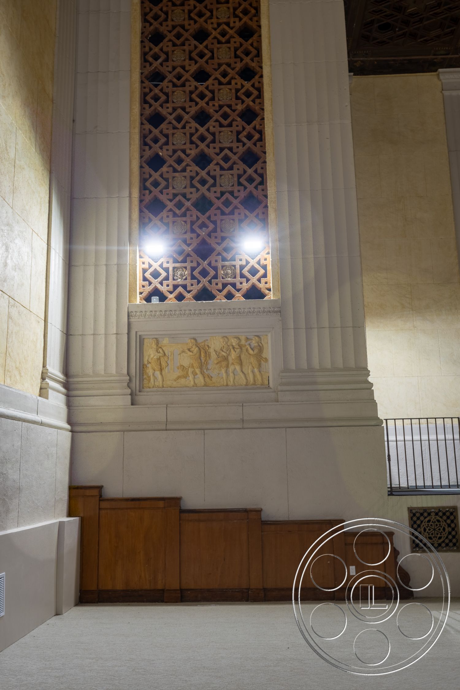 The Plaza - carpet flooring, plaster walls, textured ceiling, symmetrical layout, classical architecture, dim ambient lighting, ornate wood paneling, decorative frieze, geometric lattice work, gold detailing, columnar design, wall sculpture