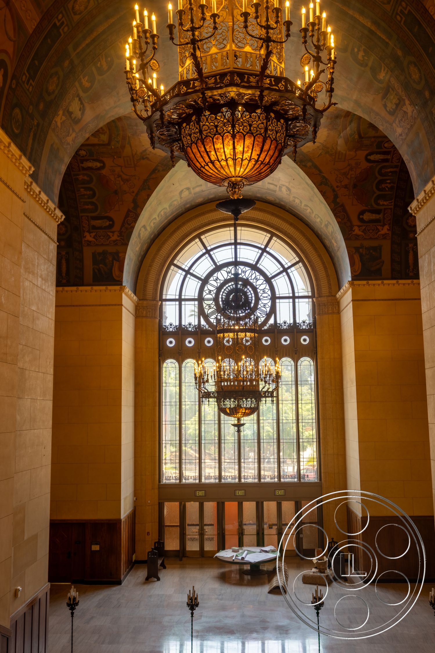 The Plaza - vaulted ceiling, marble flooring, textured plaster walls, large arched windows, symmetrical layout, classical design elements, ornate chandelier, spacious entryway, metal railing details, exposed wood paneling, art deco architectural style, decorative wall murals, geometric stained glass, gold leaf details