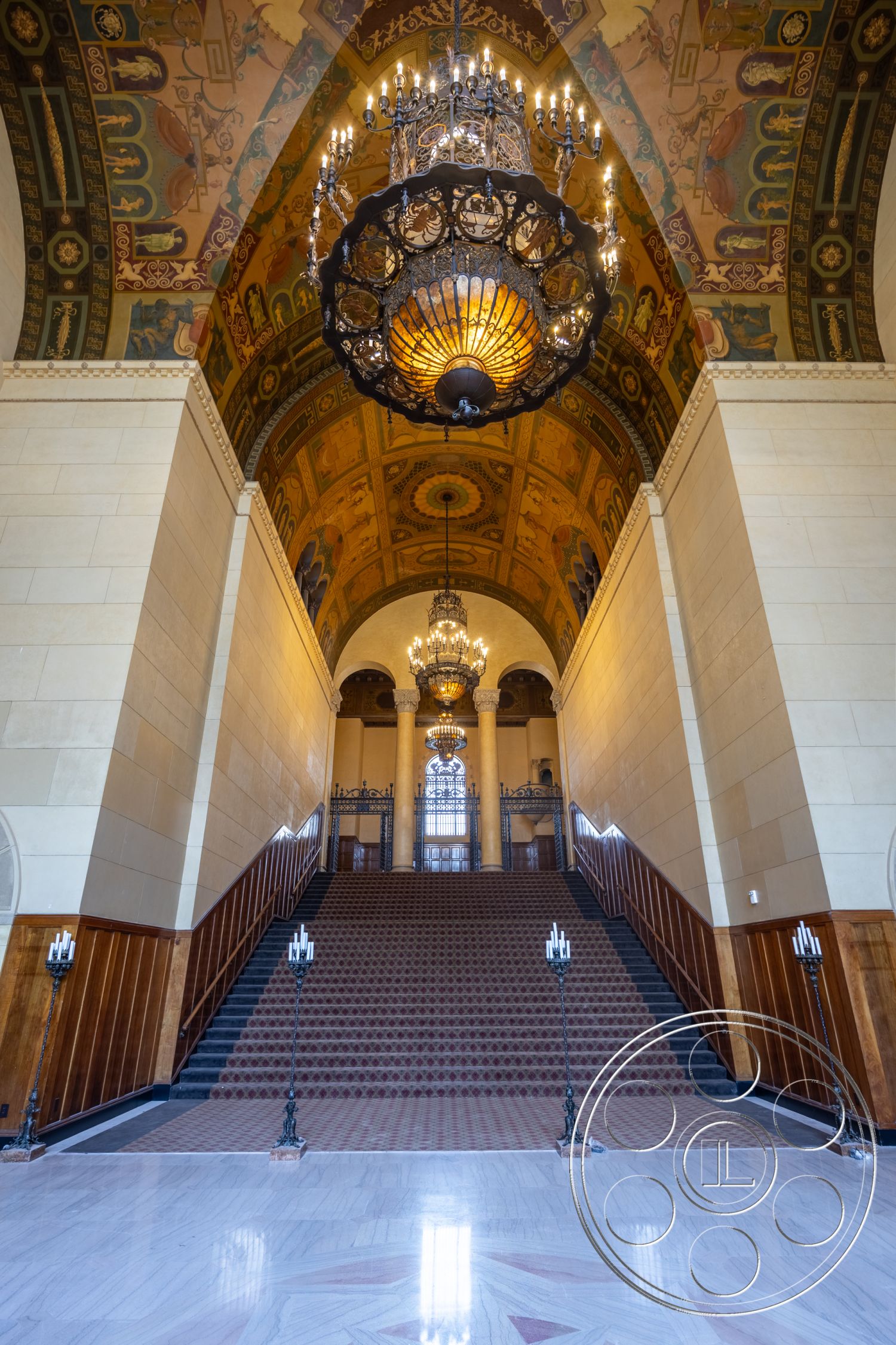 The Plaza - high ceilings, transom windows, polished marble flooring, arched doorways, grand staircase, exterior entrance, light-filled foyer, wood paneling on walls, historical architectural style, elegant interior design, ornate chandelier lighting, decorative wrought iron railings, vaulted ceiling with painted details, stair runner carpet