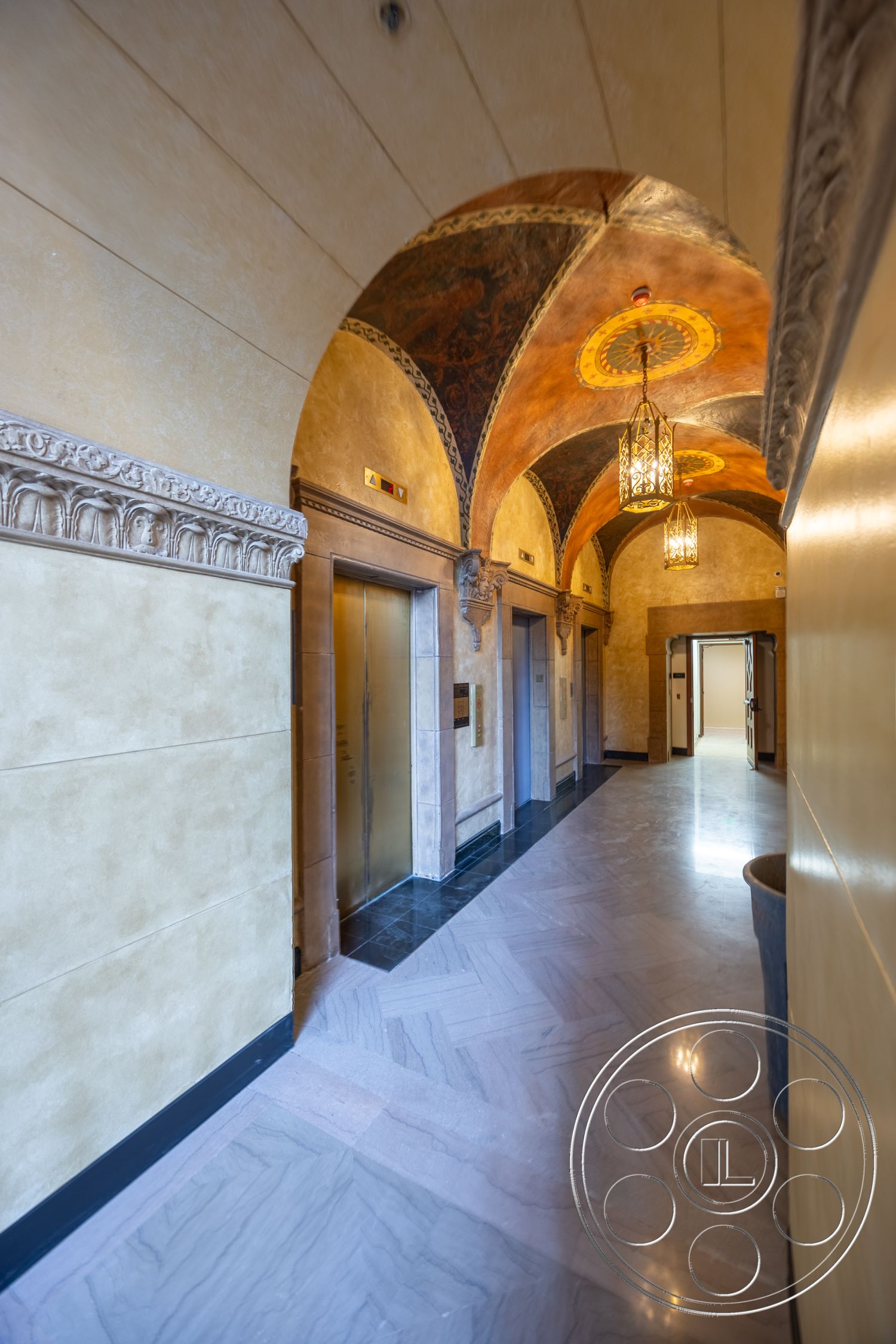 The Plaza - decorative crown molding, arched doorways, textured plaster walls, intricate wall paneling, ornate ceiling with painted details, luxury pendant lighting, polished marble hallway flooring, elevator access with a brushed metal finish, wood accents in door frames
