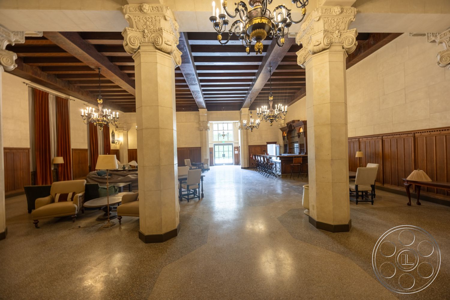 The Plaza - polished concrete floor, formal seating area, exposed wood ceiling beams, wood paneling on walls, ornate chandelier lighting, art deco architectural style, fluted column details, tall windows with drapery, integrated bar area