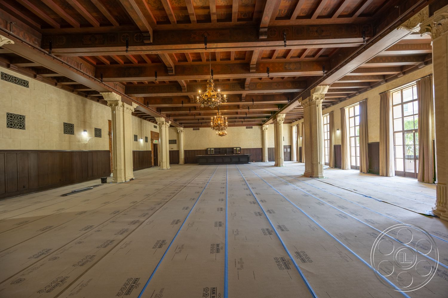 The Plaza - glass windows, plaster walls, chandelier lighting, dark wood paneling, exposed wood beam ceiling, intricate ceiling moldings, stone accent pillars, unfinished flooring