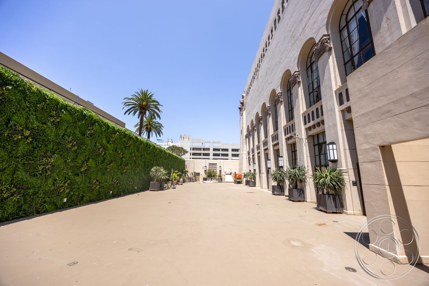 The Plaza - large windows, exterior, palm trees, concrete planters, urban environment, arched windows, paved courtyard, commercial architecture, stucco building facade, decorative stone detailing, modern landscaped wall