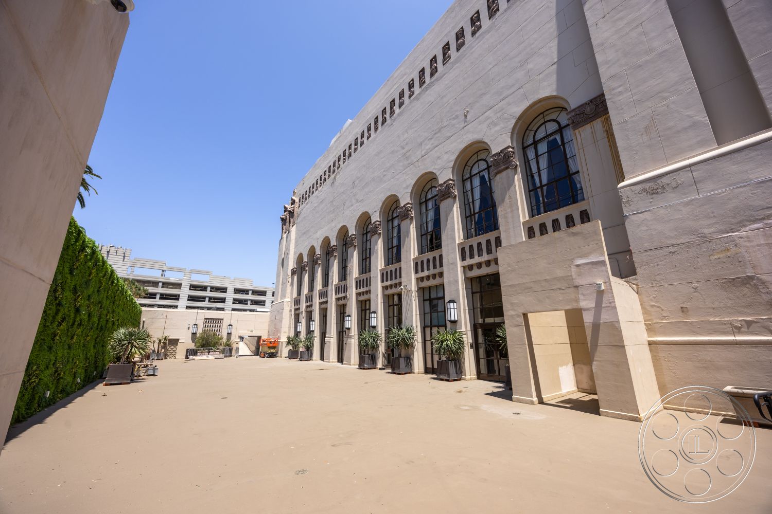The Plaza - exterior, high ceiling, arched windows, paved courtyard, stucco wall finish, landscape planter with greenery, open courtyard space, ornate window details, commercial building architecture, decorative stone cornice, planted vertical garden, Art Deco architectural style