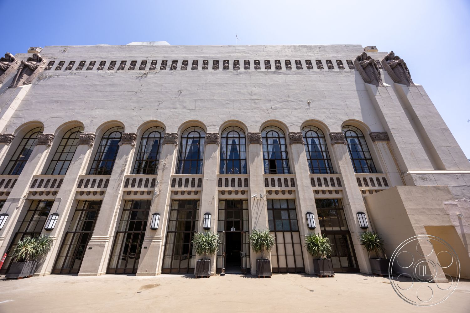 The Plaza - exterior, symmetrical facade, large arched windows, black metal window frames, stucco wall finish, built-in planters, historic architectural style, ornate stone detailing, decorative stone reliefs, tall entryway, modern outdoor light fixtures