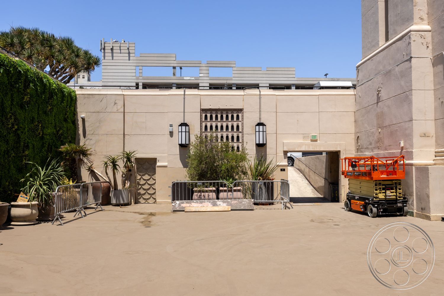 The Plaza - exterior, concrete pathway, high ceiling, urban setting, arched doorway, stucco wall finish, modern wall sconces, minimalist architectural style, landscaped tropical plants, decorative stone paneling, outdoor paving stones, metal scaffolding