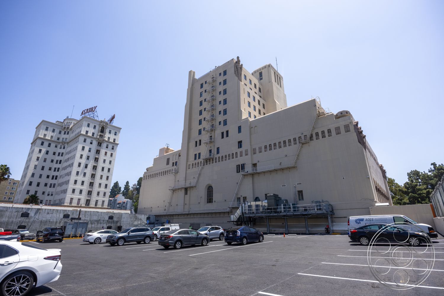 The Plaza - exterior, flat roof, industrial elements, urban environment, rectangular windows, metal railing systems, concrete building facade, historic architectural style, multi-story structure, urban skyline setting, parking lot surface, brick exterior accent details, paved asphalt lot