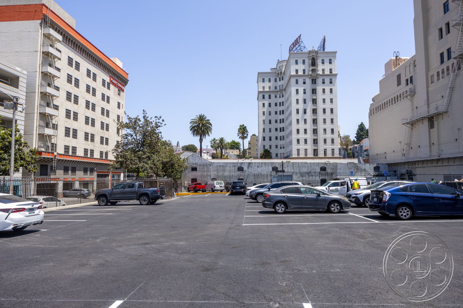 The Plaza - urban setting, glass windows, multi-story building, modernist architecture, concrete parking lot, flat roof design, stucco exterior walls, brick building facade, steel staircases, palm trees in surroundings, historical building details, exposed metal fire escape