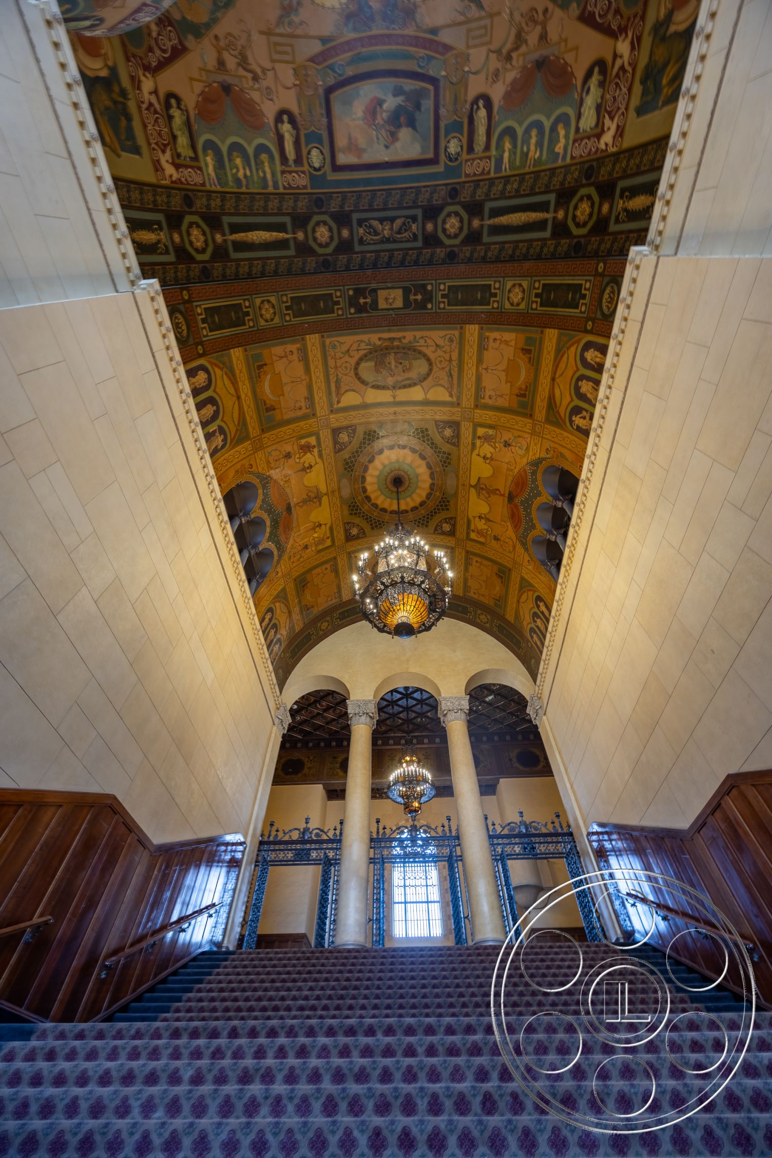 The Plaza - exterior, chandeliers, large arched windows, wood paneling on walls, decorative wall moldings, historical architectural style, vaulted entryway ceiling, intricate wrought iron railings, ornate painted ceiling, marble stair treads, carpeted staircase risers, columns with ornate capitals