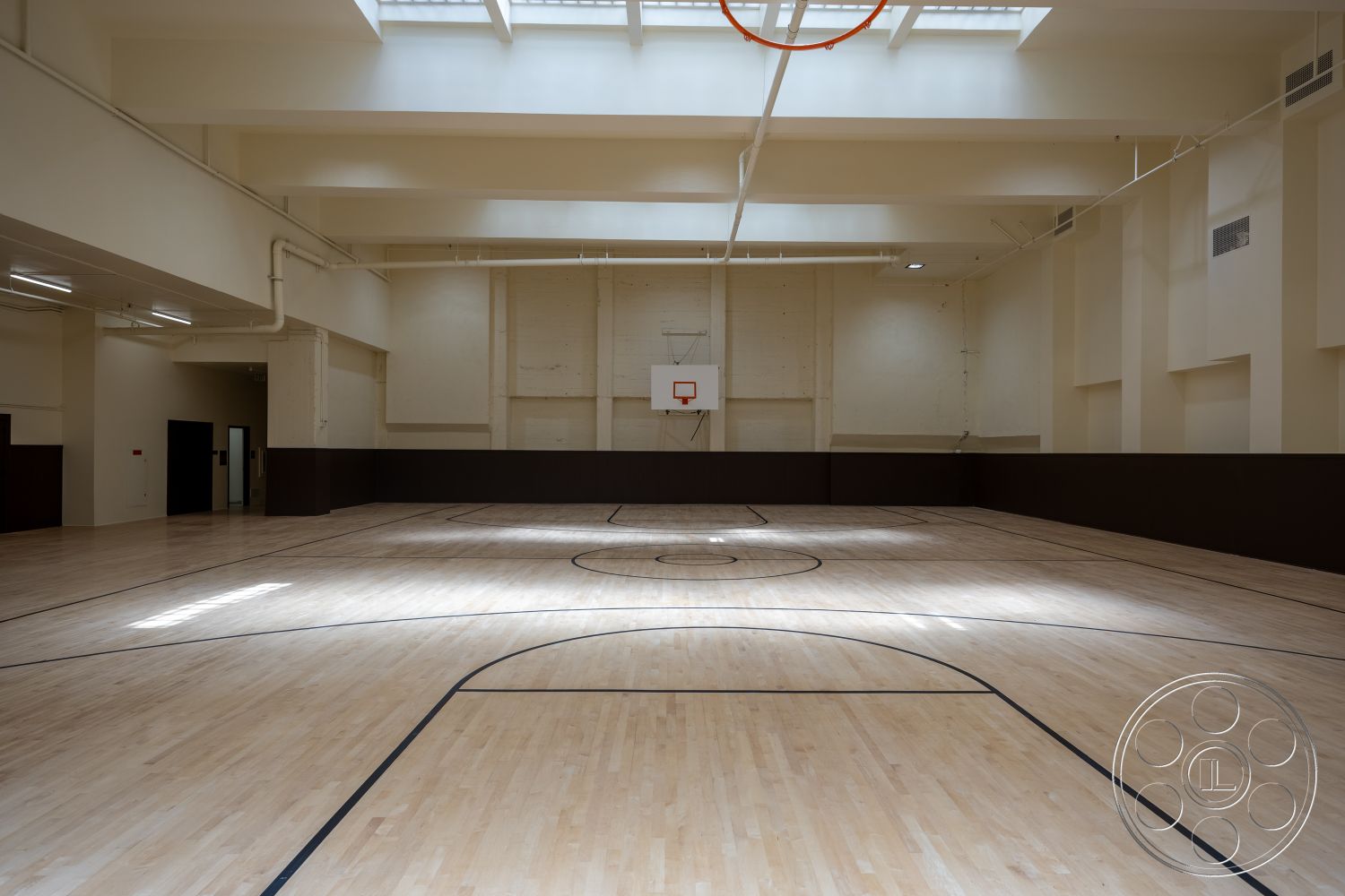 The Plaza - dark wood paneling, exposed ceiling beams, white painted walls, high ceiling with skylights, open gym layout, interior hardwood basketball court flooring, round basketball hoop, floor markings for basketball court