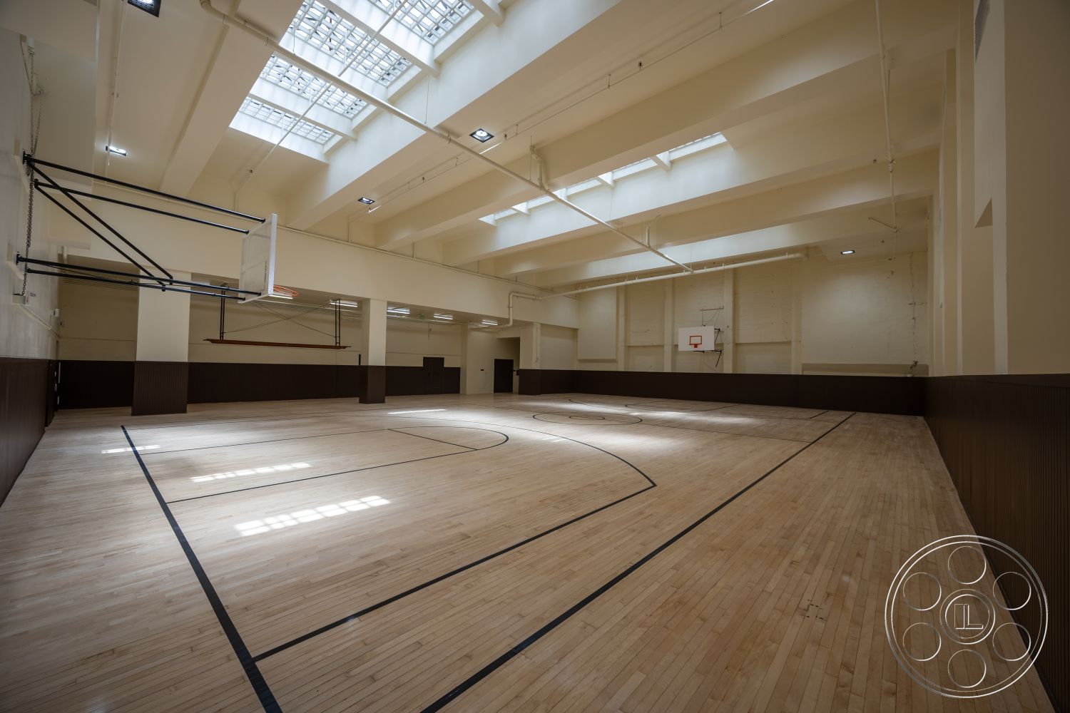 The Plaza - exposed beam ceiling, open space layout, dark wood paneling, industrial ceiling lights, light-colored painted walls, maple hardwood gym floor, interior gymnasium, side wall basketball hoop, skylight roof panels, full court basketball layout