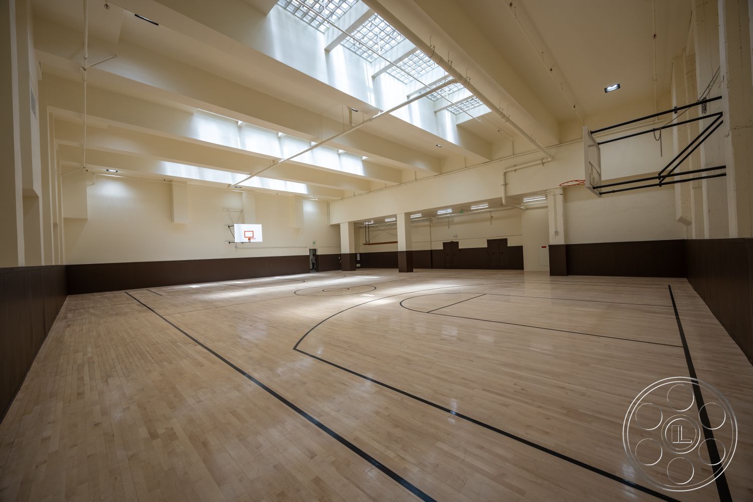 The Plaza - exposed ceiling beams, high ceiling with skylights, basketball hoop installation, hardwood gymnasium floor, light beige interior walls, dark wood paneling wall treatment, interior recreational space