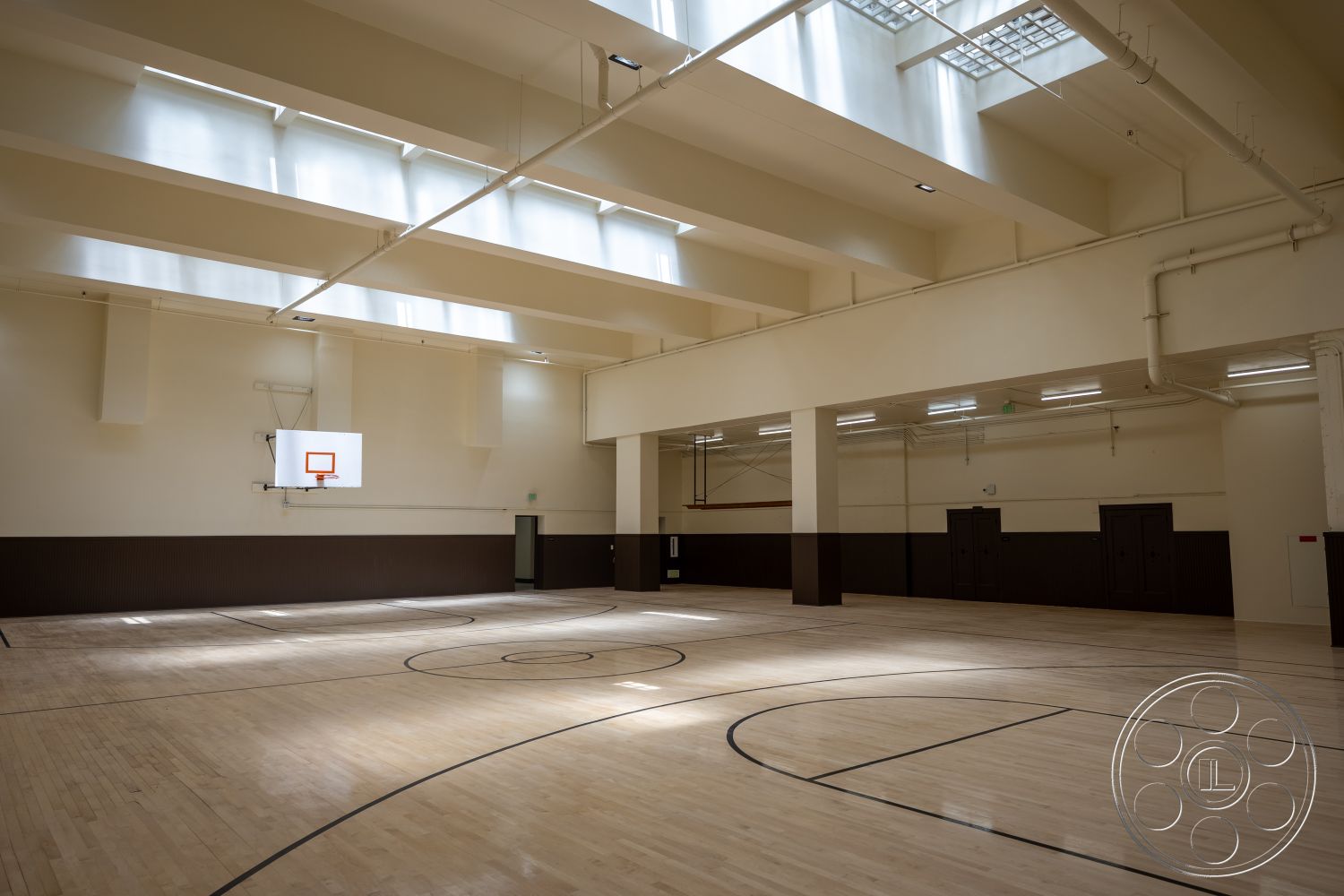 The Plaza - industrial lighting fixtures, skylights, dark wood paneling, exposed ceiling beams, white painted walls, hardwood gymnasium floor, interior gymnasium, basketball court with three-point line