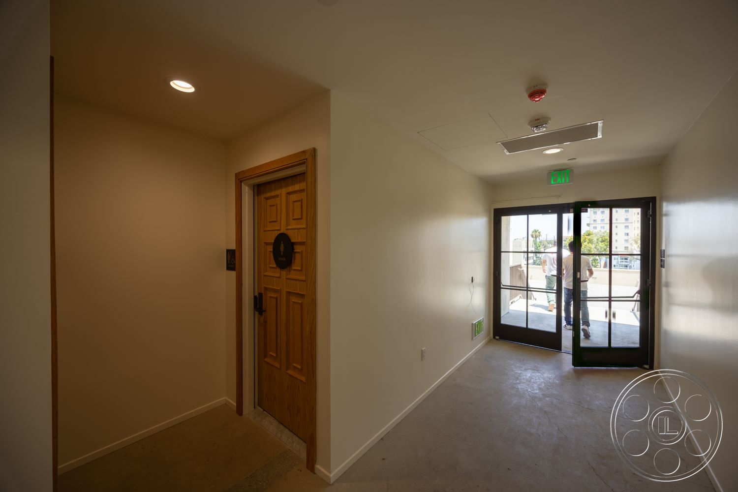 The Plaza - open floor plan, concrete floor, recessed ceiling lights, interior hallway, exit signage, light beige painted walls, solid wood door with decorative panels, double glass patio doors, wood trim around doors, modern exit door design