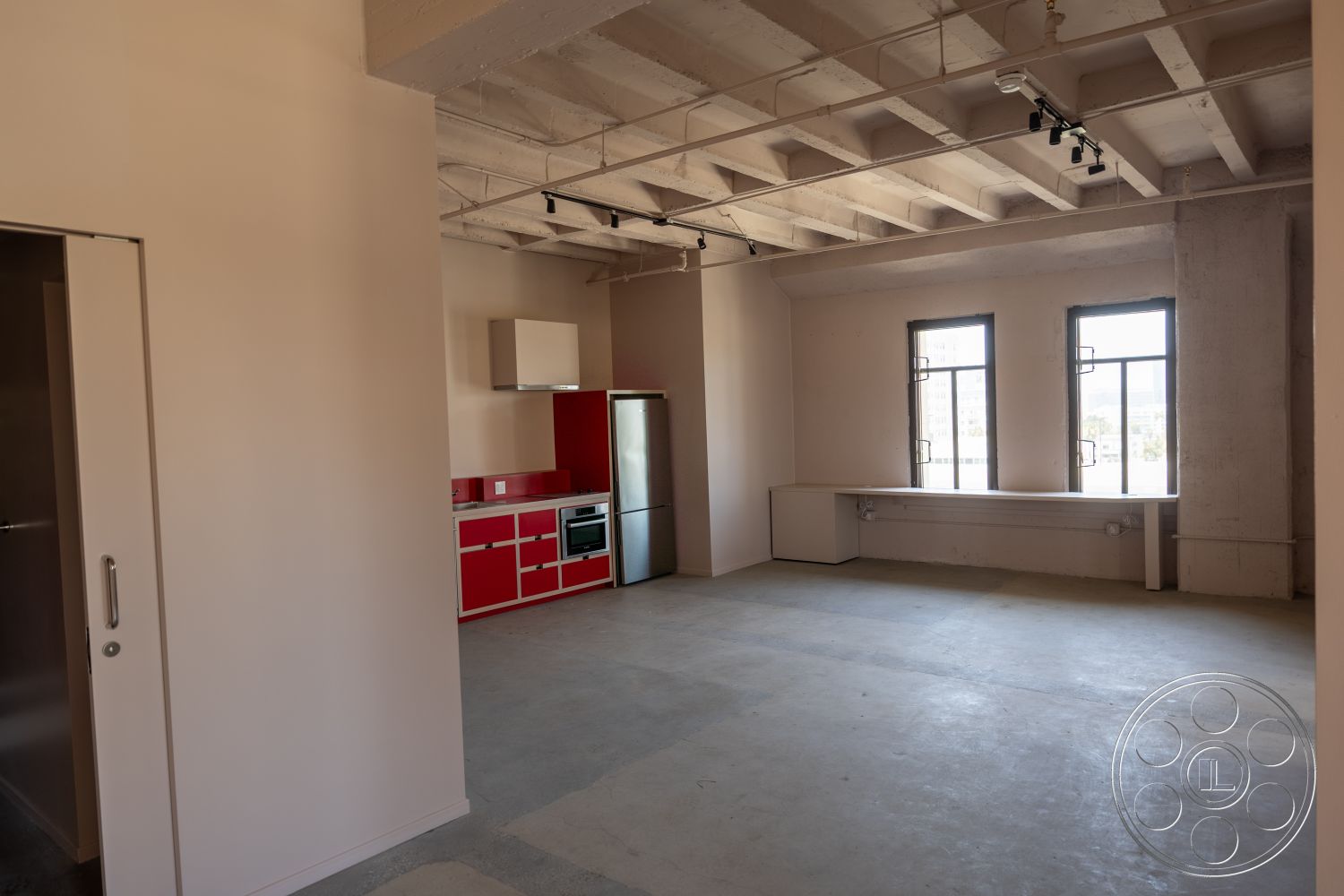 The Plaza - large windows, neutral wall colors, minimalist aesthetic, open concept layout, industrial style, track lighting, concrete floors, exposed concrete ceiling, stainless steel refrigerator, modern kitchen design, red kitchen cabinets, built-in countertop