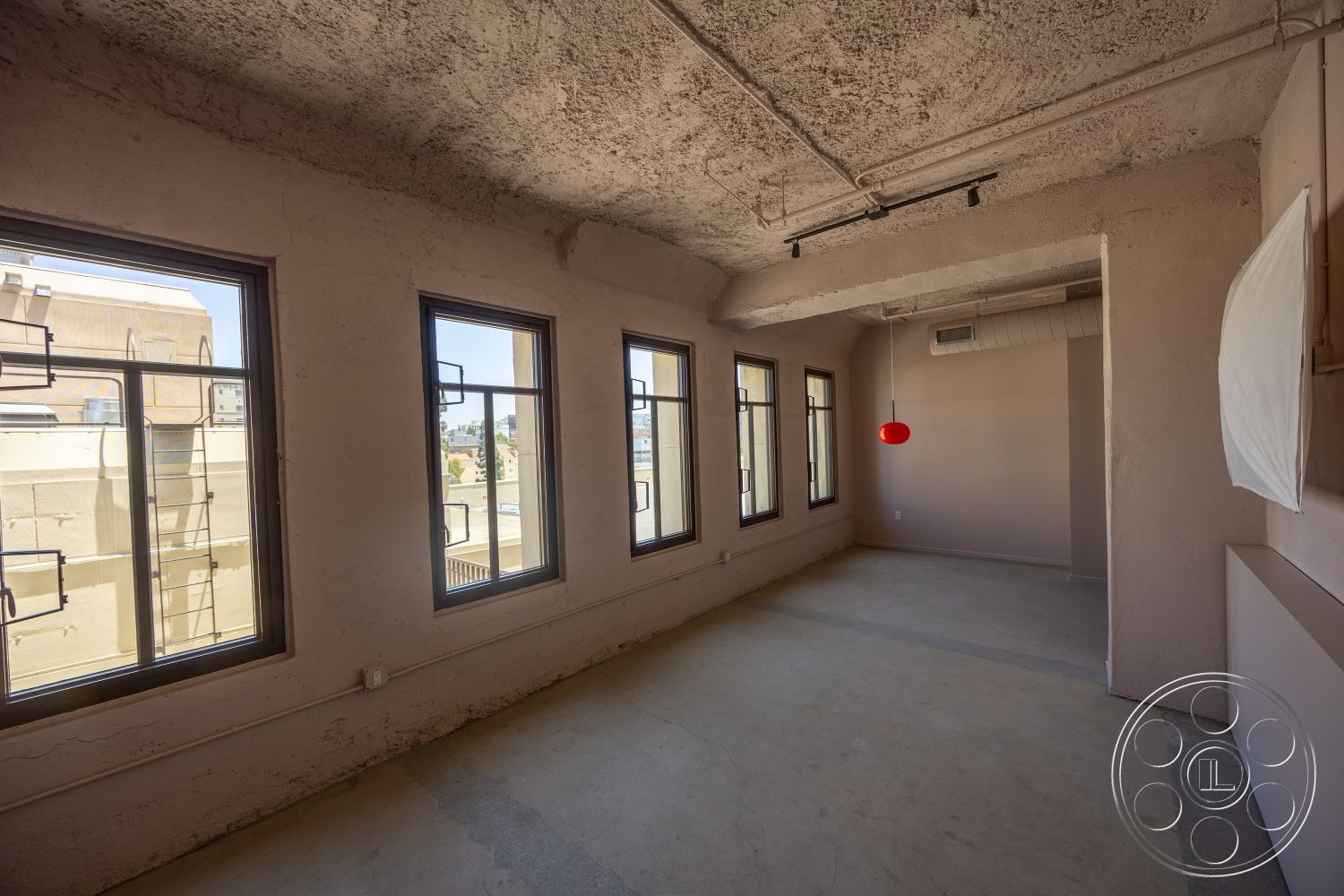 The Plaza - neutral color palette, large windows, natural light, open floor plan, concrete flooring, modern pendant lighting, exposed concrete walls, textured plaster ceiling, minimalist interior, industrial windows, urban loft space, ceiling ventilation duct, corner ducted air conditioning unit